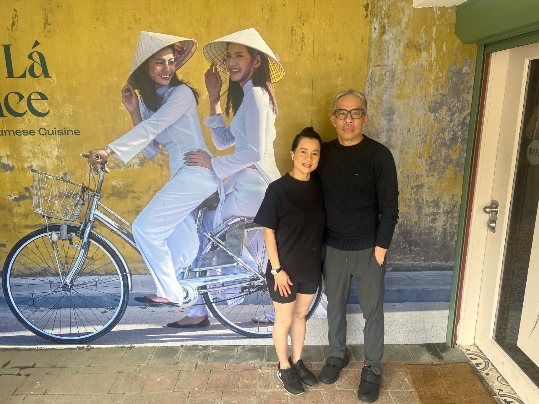The family owners of Nón Lá Palace standing in front of the restaurant's Vietnamese mural